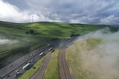 Aerial view of highway through green hills with wind turbines